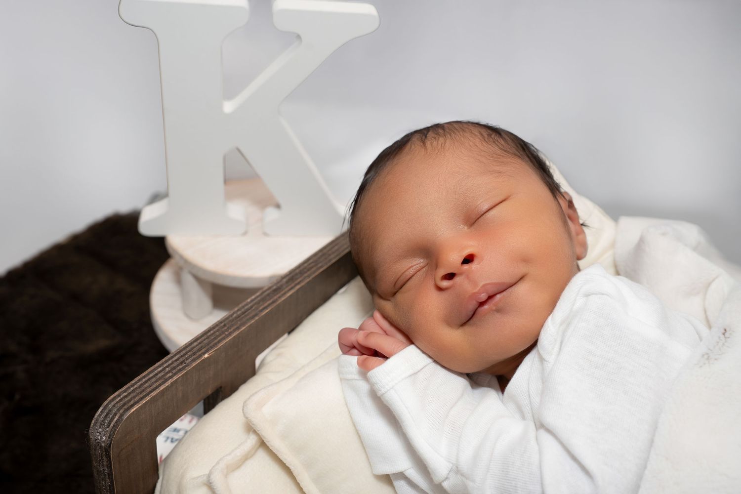 Close-up of sleeping newborn baby with soft smile resting in wooden crib with letter K.