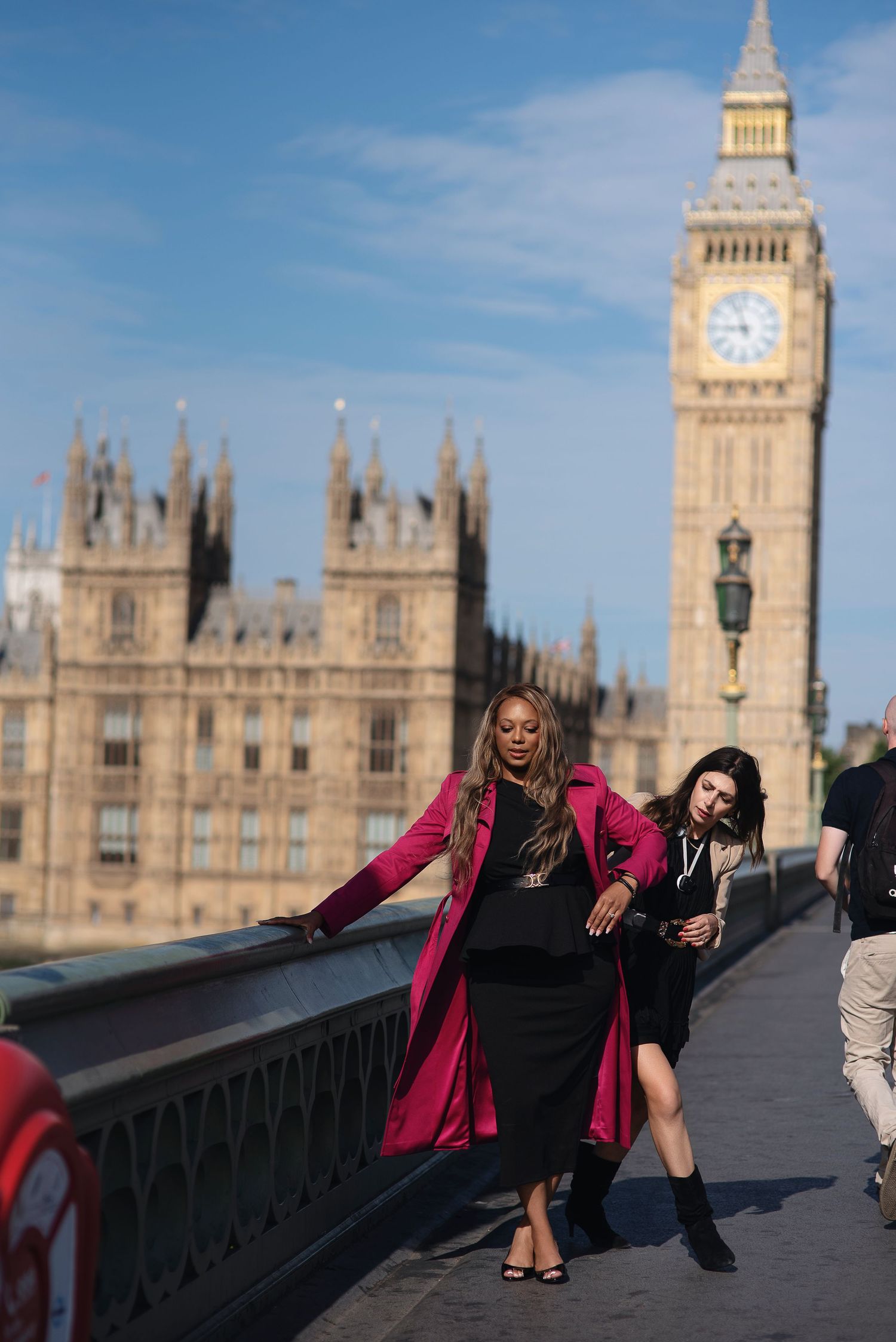 Two stylish women pose on Westminster Bridge with Big Ben and Houses of Parliament in London backdrop.