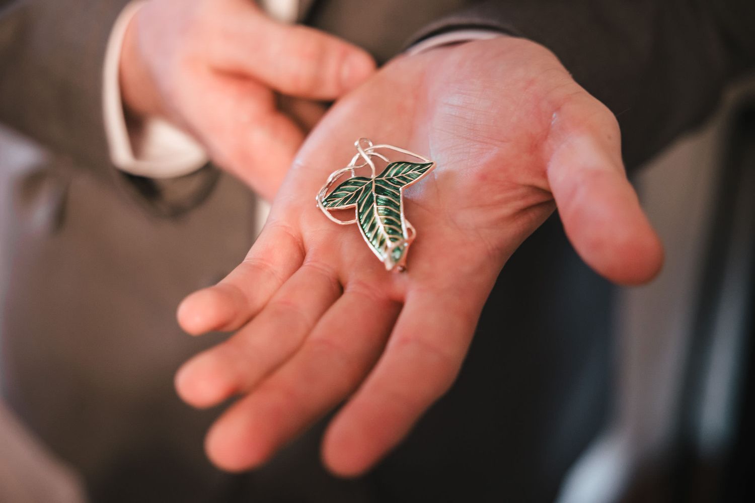 Close-up of an unwrapped elf leaf pin held in a groomsman's open palm at Searles Castle.