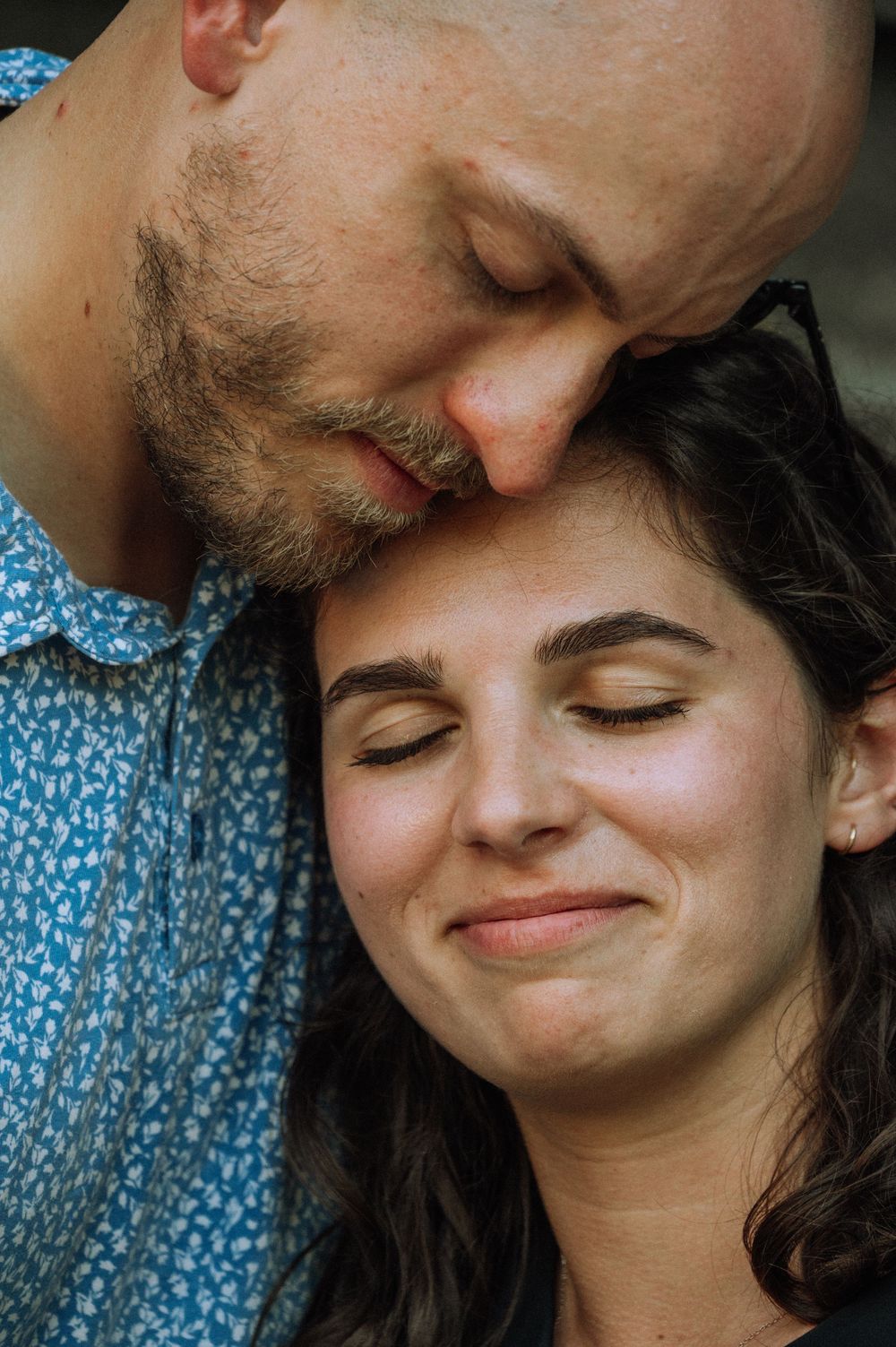 A man tenderly kisses a smiling woman on the forehead in a close romantic portrait.