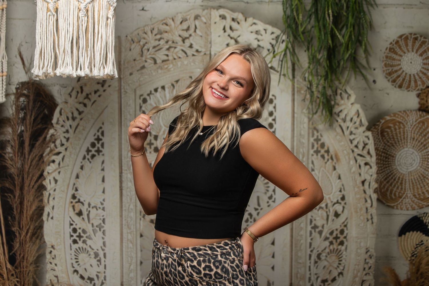 Young blonde woman posing in black crop top and leopard print skirt in boho-styled photo studio.
