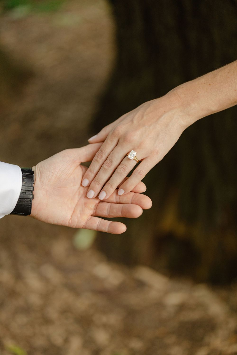Close-up of bride and groom holding hands, showcasing a delicate diamond engagement ring on the bride's hand.
