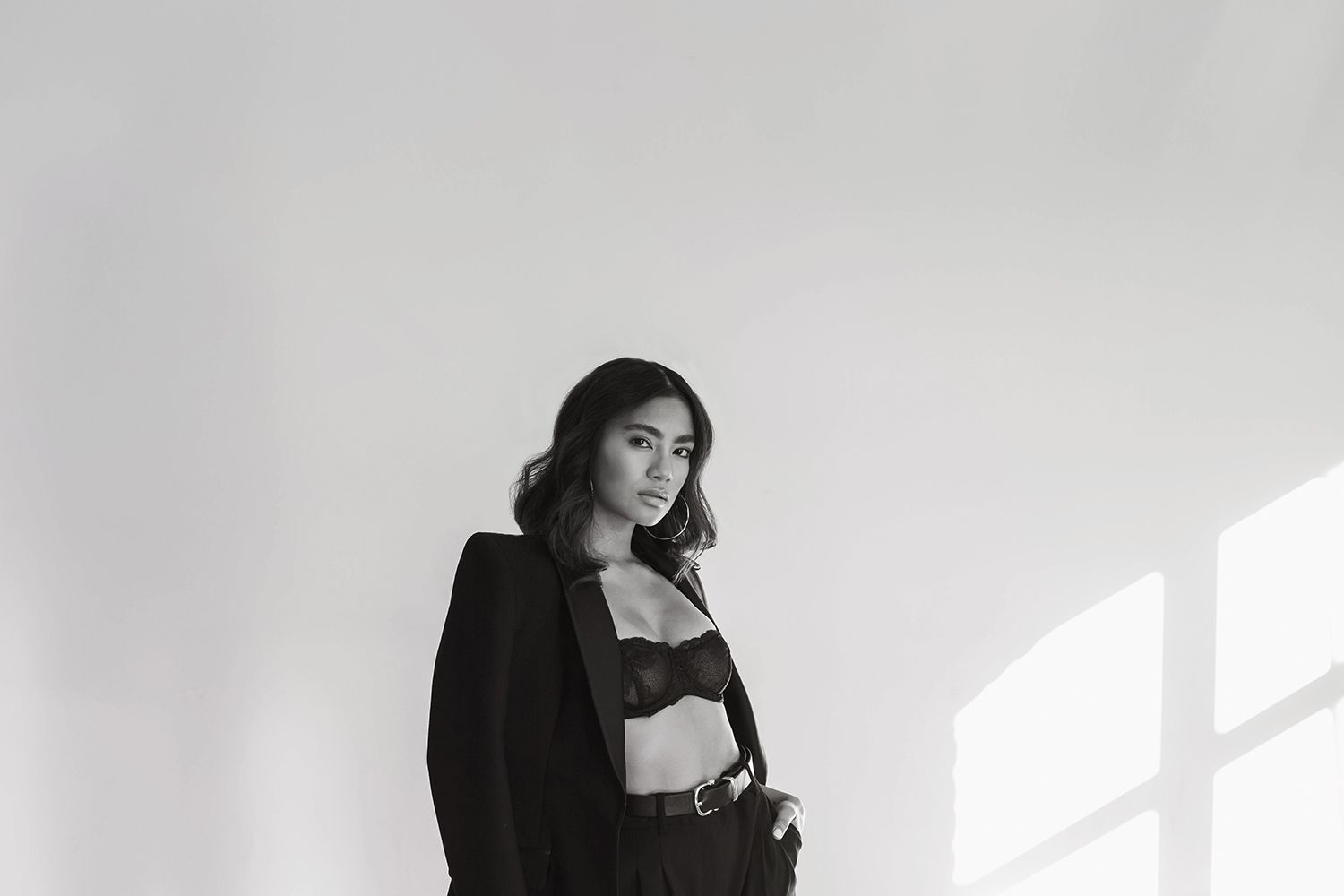 A fashion portrait in black and white featuring someone in a dark blazer against a bright window.