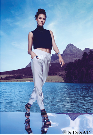 ST&SAT model in black crop top and white pants wearing strappy heels by mountain lake.