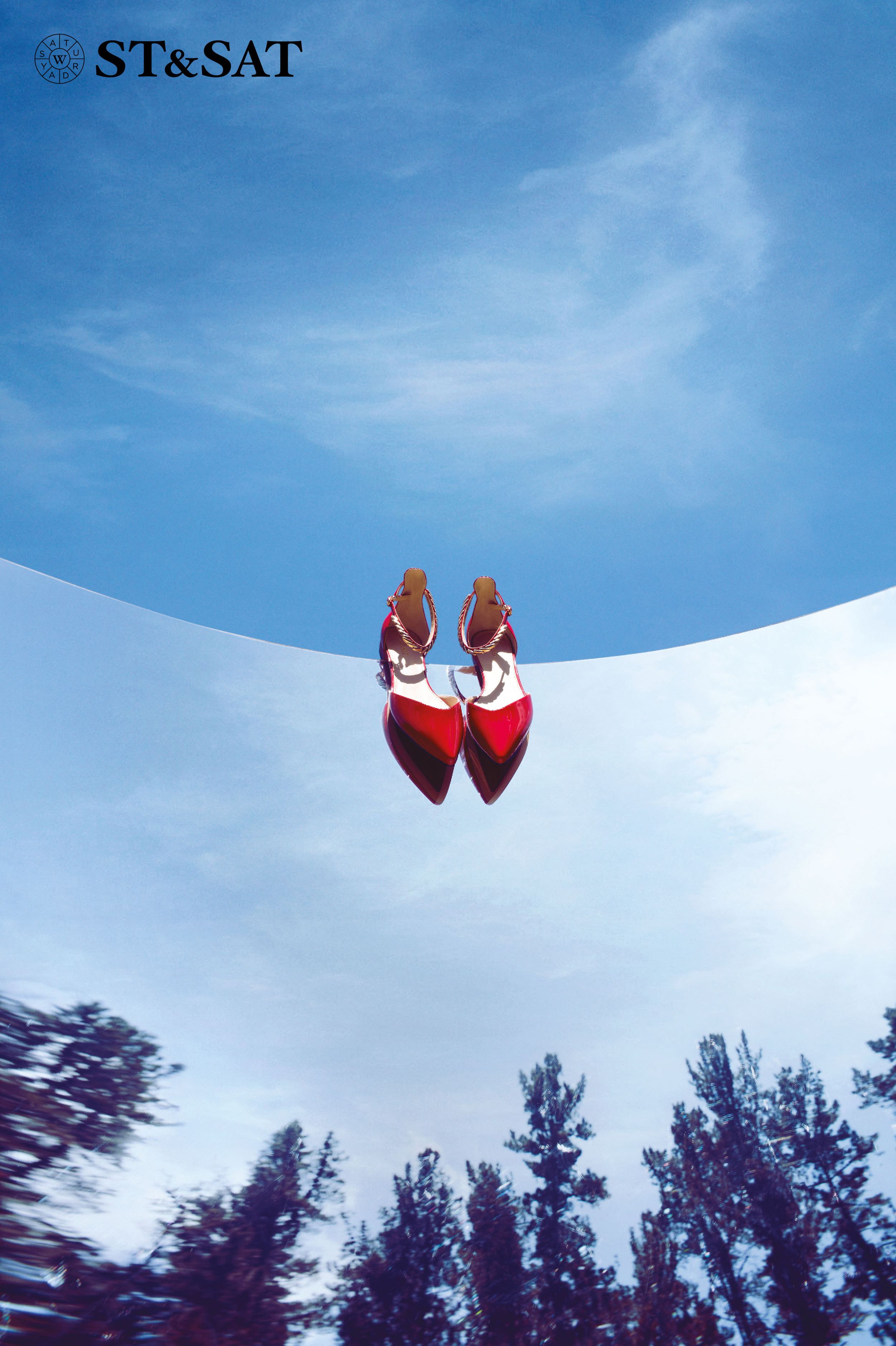 ST&SAT red pointed-toe heels floating against a bright blue sky with trees reflected below.