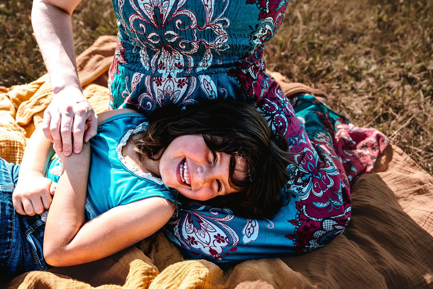 A smiling child with braces lies on a colorful blanket outdoors, cradled in an adult's lap during a family photo session.