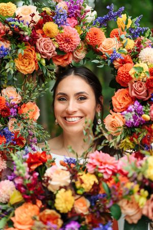 Smiling bride framed by vibrant colorful floral arrangement with orange, pink, and purple flowers.