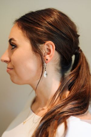 Woman with dark hair in ponytail wearing elegant crystal drop earrings and gold necklace, side profile view.