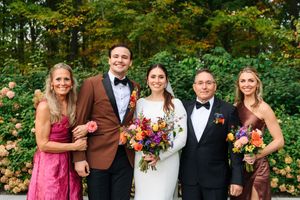 Wedding party of five posing outdoors, bride holding colorful bouquet, guests in formal attire with lush green backdrop.