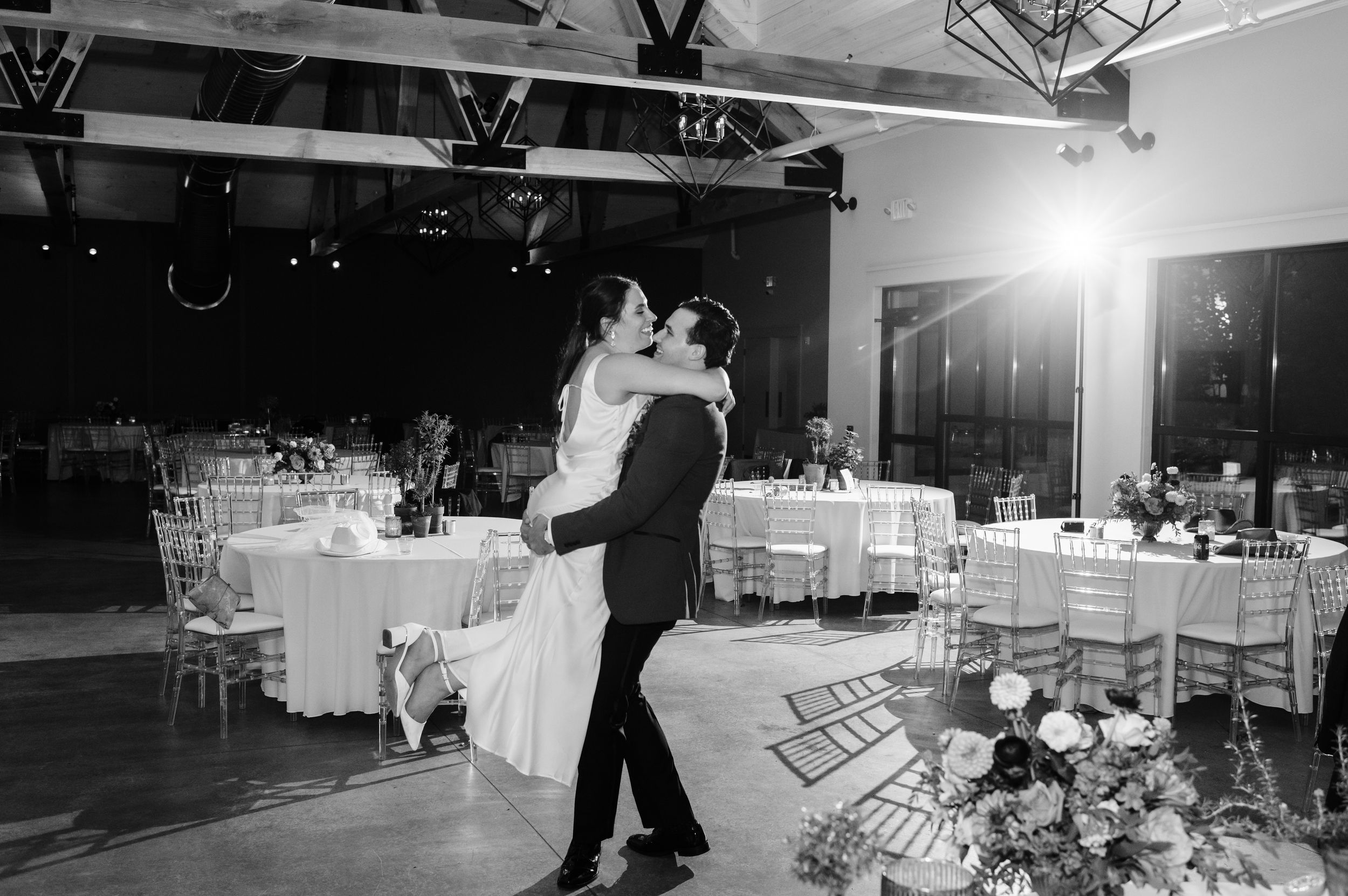 Black and white photo of groom lifting bride during first dance at elegant wedding reception.