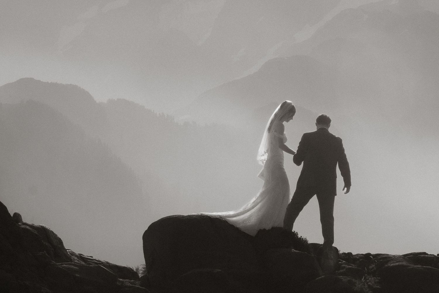 Two figures stand in a mountain meadow filled with white wildflowers at sunset.