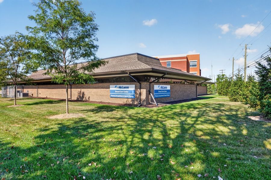 Single-story commercial building with blue signage on a green lawn surrounded by mature trees on a sunny day.