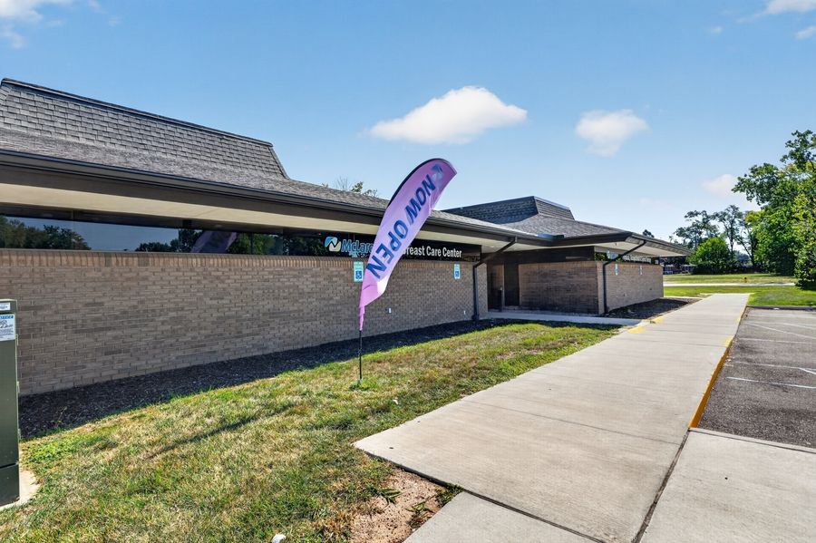 Modern brick medical care facility exterior with a colorful promotional flag banner on a sunny day.