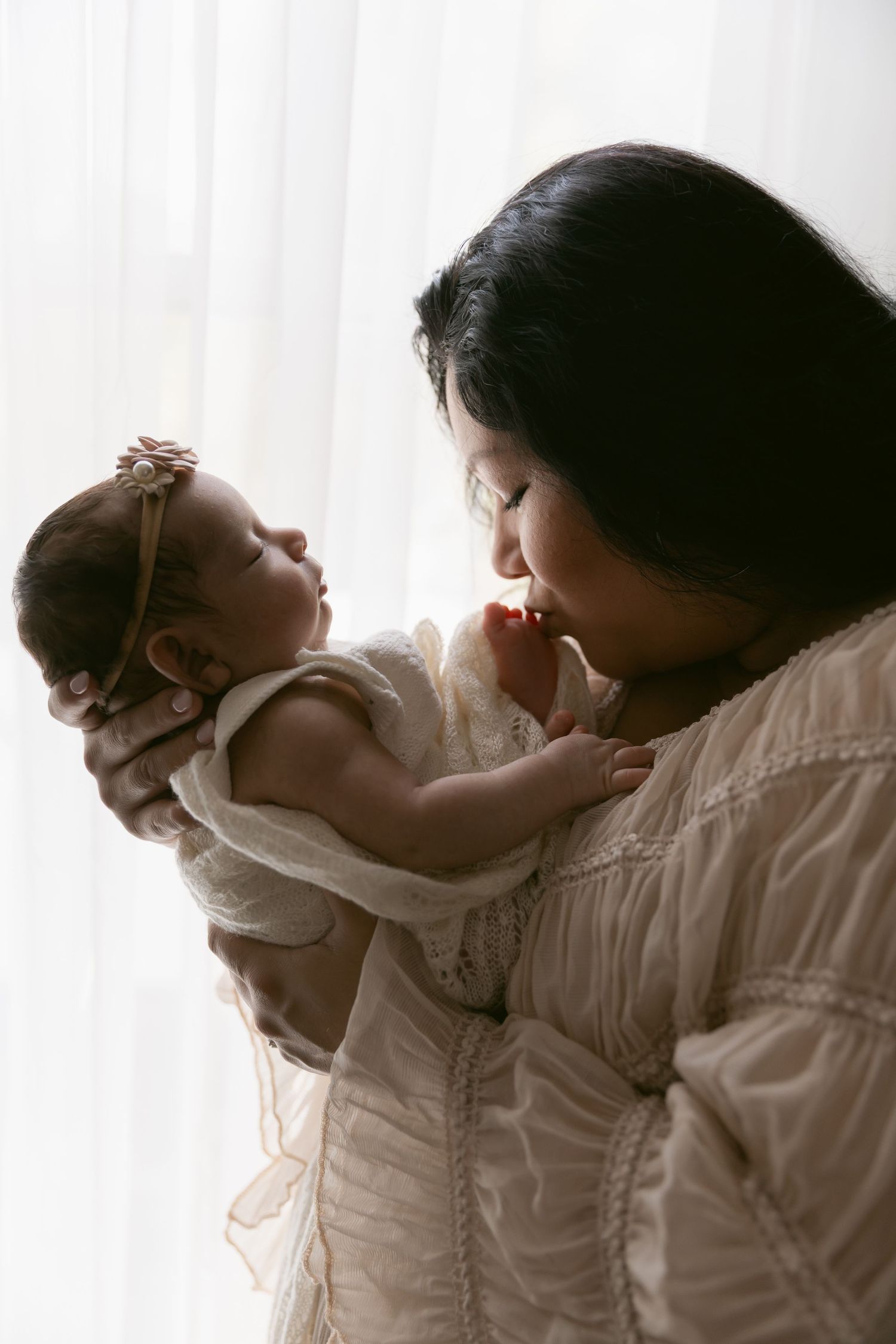 Mother holding newborn baby in a soft silhouette created with natural window light during an East Texas newborn photography Session in Tyler