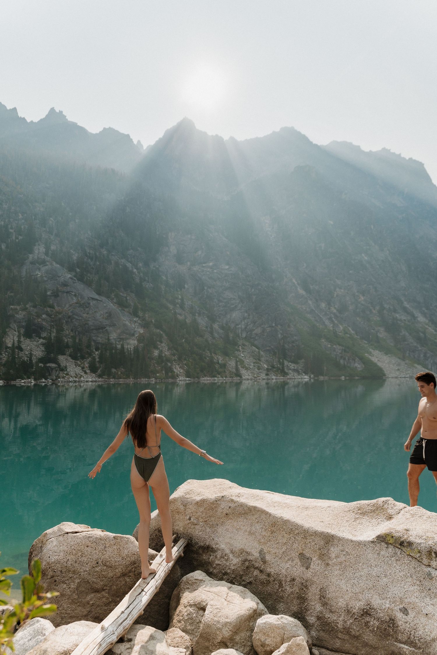 Two people swimming in a turquoise alpine lake surrounded by misty mountain scenery.