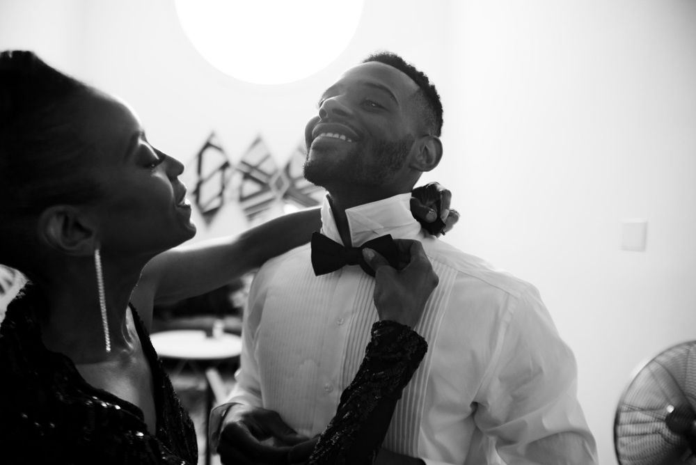 Black and white candid moment showing bowtie adjustment with joyful laughter.