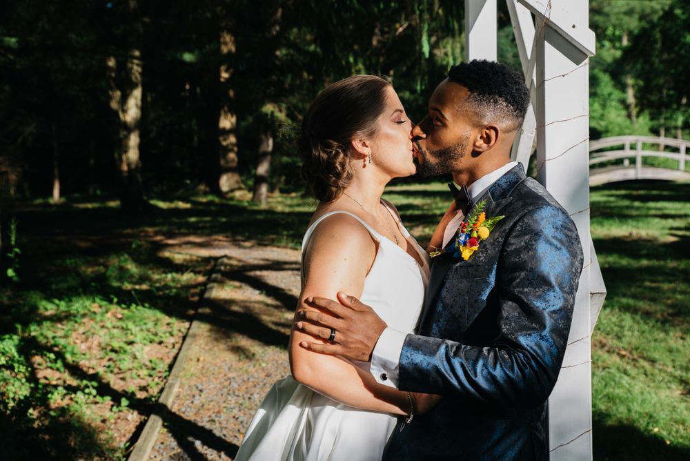 Intimate outdoor wedding moment captured in natural sunlight against garden backdrop.