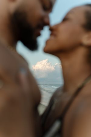 Romantic couple sharing a tender kiss on the beach with ocean waves and clouds in the background.