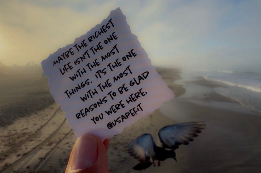 Hand holding a note card on a beach at sunset with an inspirational quote and a bird flying nearby.