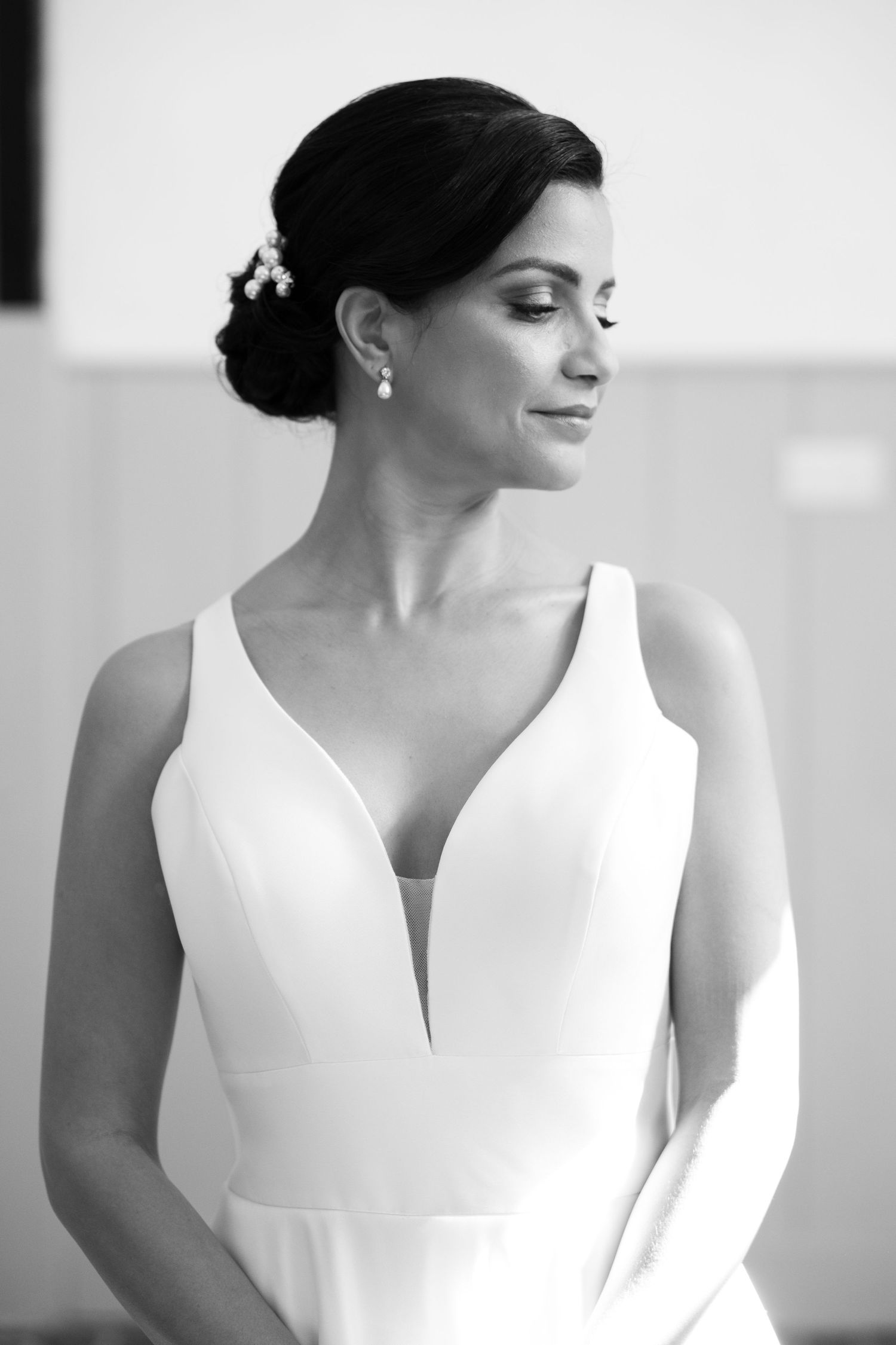 Black and white portrait of a bride in a deep V-neck wedding gown with pearl hair accessories and drop earrings.