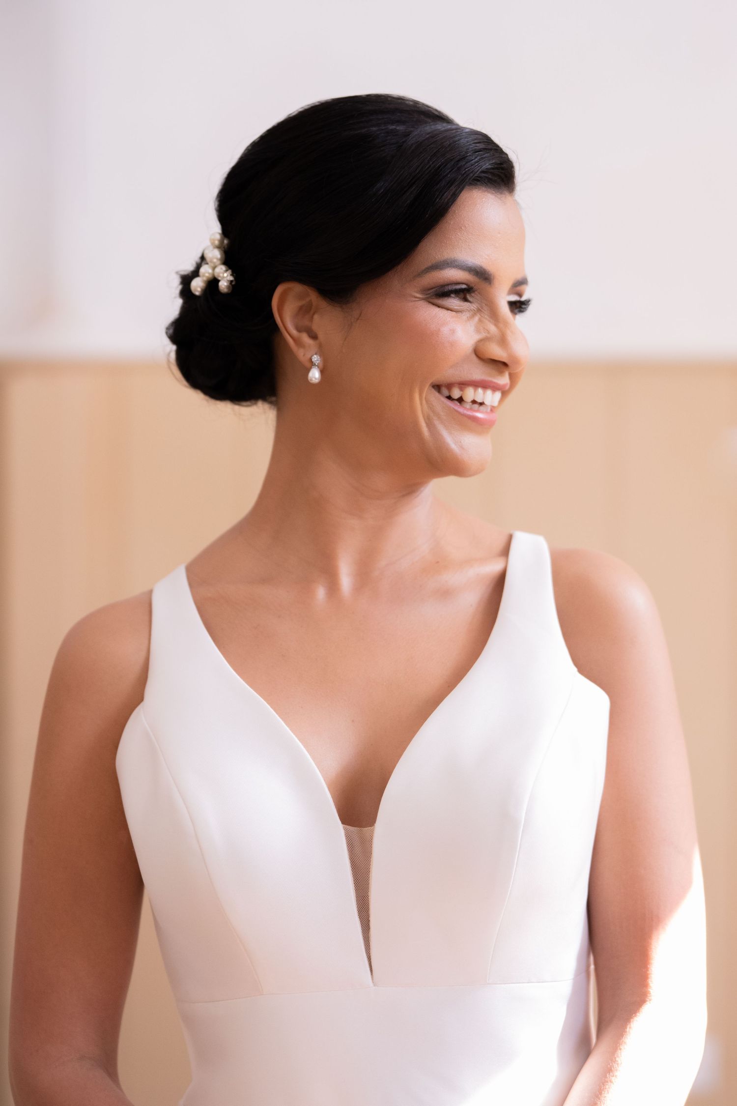 Smiling bride in a white V-neck gown with pearl hair accessories and drop earrings on her wedding day.