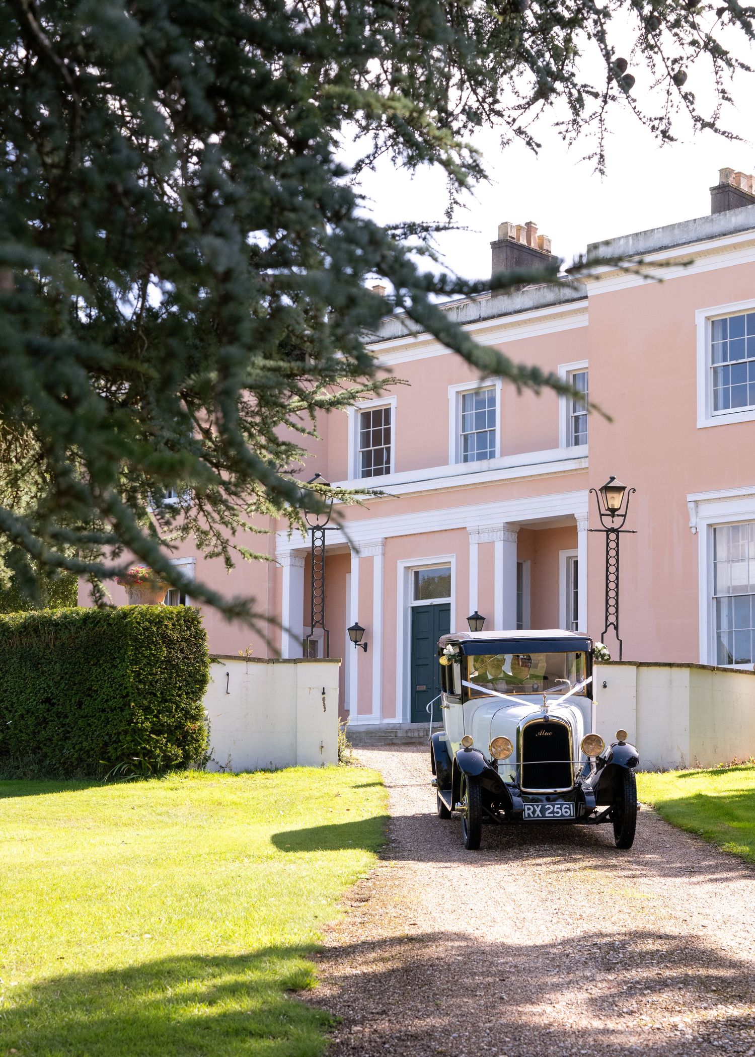 Vintage classic car parked on gravel driveway outside elegant pink Georgian country house wedding venue.