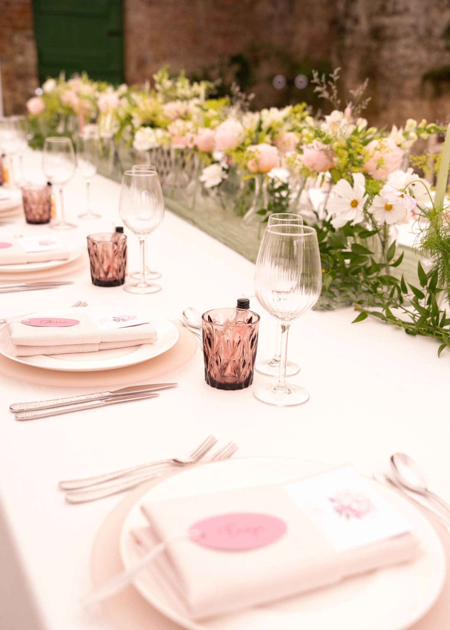 Elegant wedding table setting with pink floral centerpiece, crystal glasses, and white napkins with pink accents.
