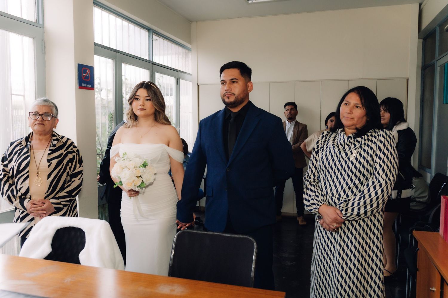 Bride and groom stand with two female witnesses during indoor civil wedding ceremony.