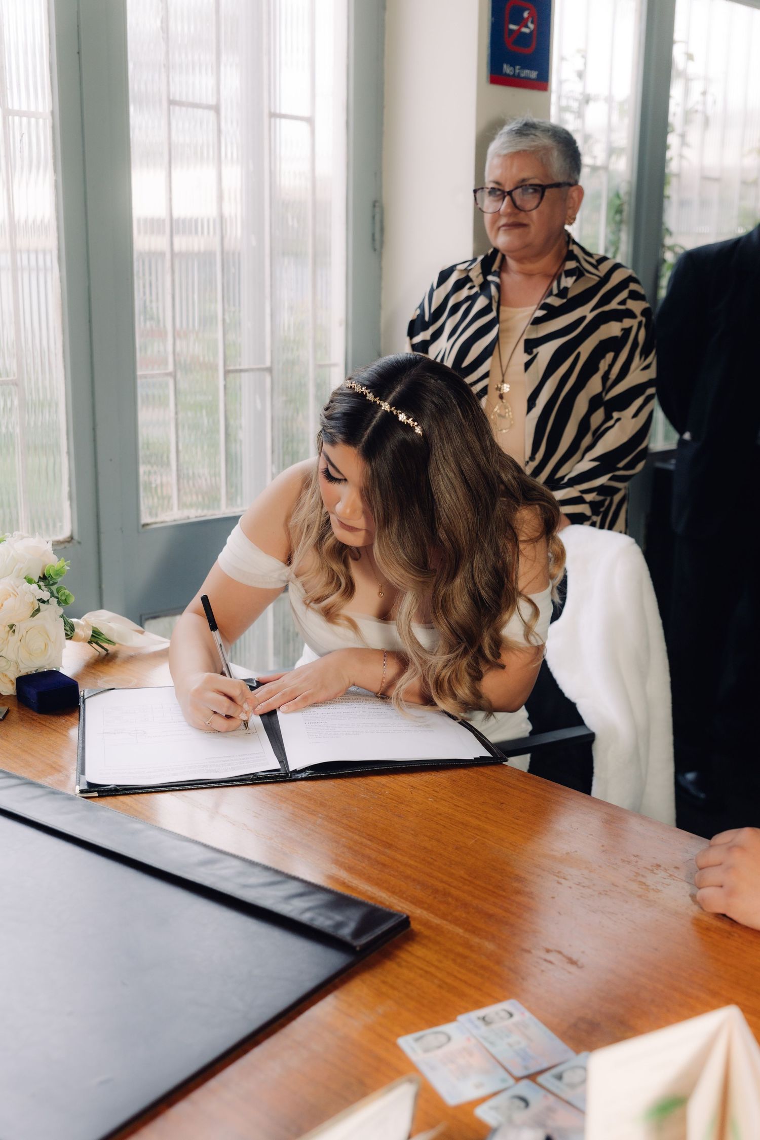 Bride signing marriage certificate at wooden desk during civil wedding ceremony.