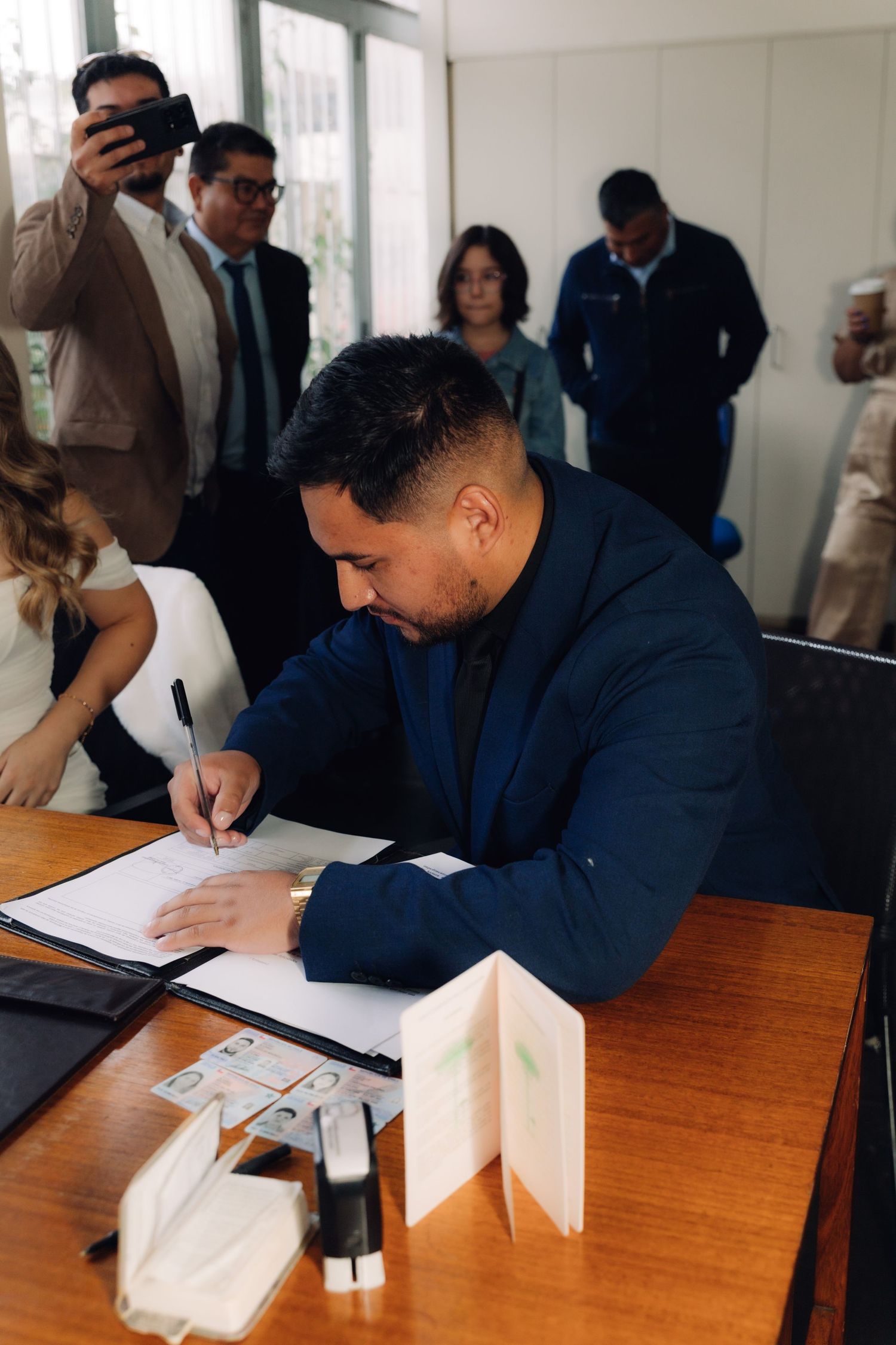 Groom in navy suit signing marriage documents at civil wedding ceremony.