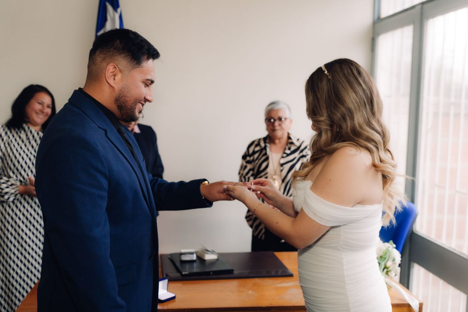Smiling groom exchanging wedding rings with bride at civil marriage ceremony.