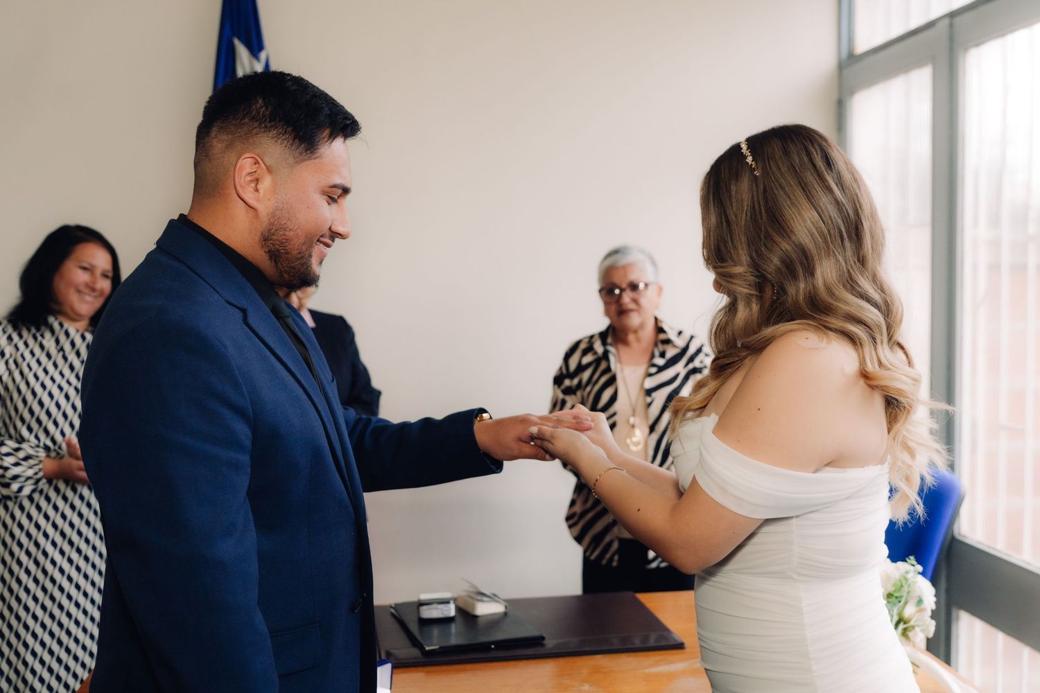 Groom holding brides hand during wedding ring exchange at civil ceremony.