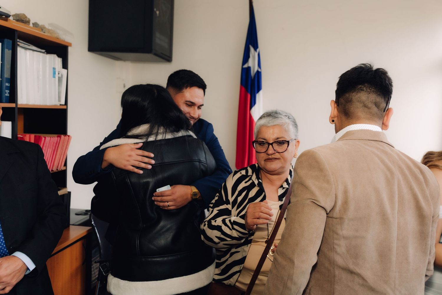 Newlywed groom embraces guest as family gathers to celebrate after Chilean civil ceremony.