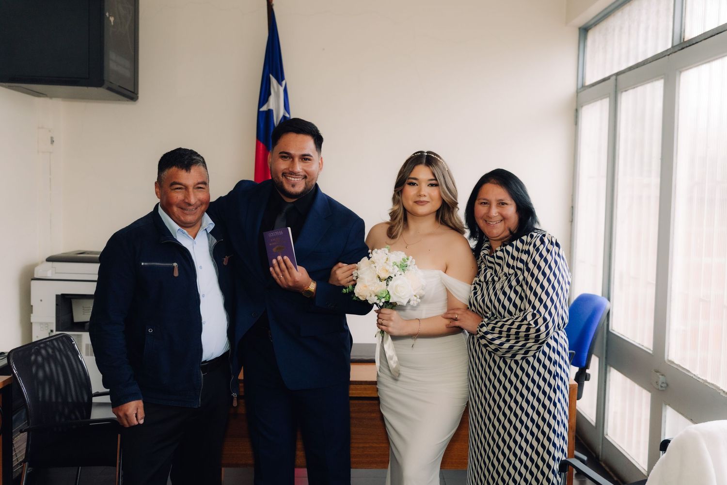 Smiling newlywed couple poses with parents holding bouquet and certificate at Chilean wedding.
