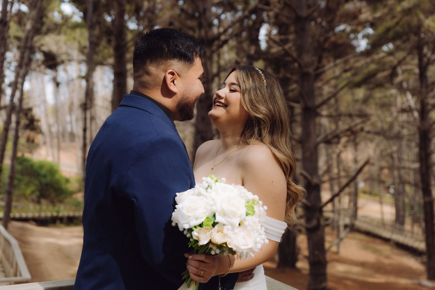 Bride and groom share a romantic moment in a forest, bride holding white bouquet in wedding attire.