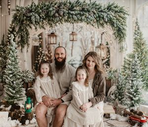 Family of four posing for a festive Christmas photo surrounded by snowy trees and holiday decorations.