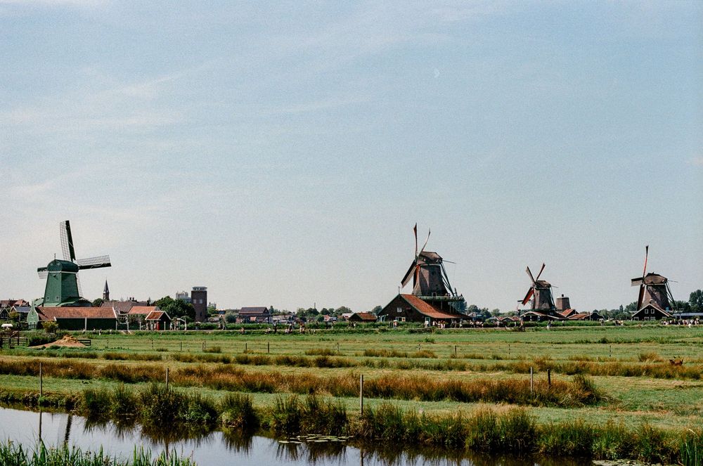 Traditional Dutch windmills at Zaanse Schans along green fields and a calm river.
