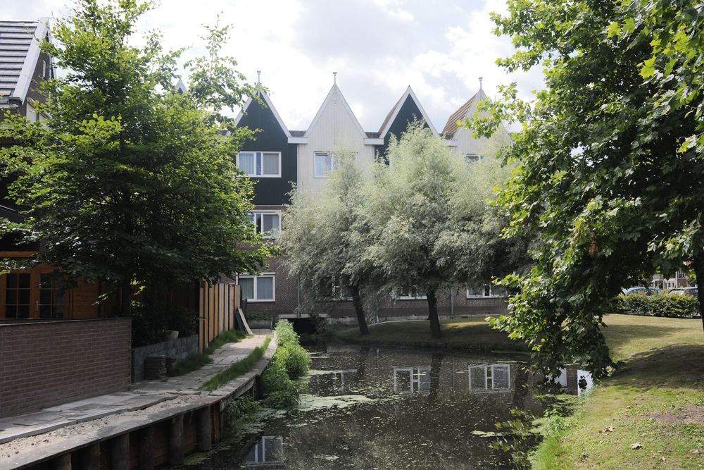 Canal reflecting trees and Dutch-style houses with pointed roofs on a sunny day in a peaceful residential neighborhood.