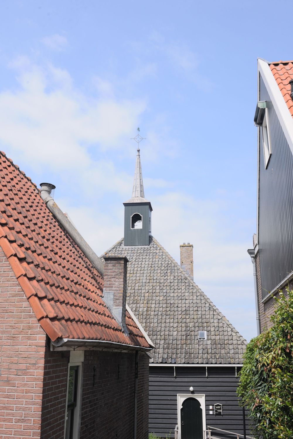 Historic Dutch church with a pointed steeple and weather vane, surrounded by traditional brick and wooden buildings under a blue sky.