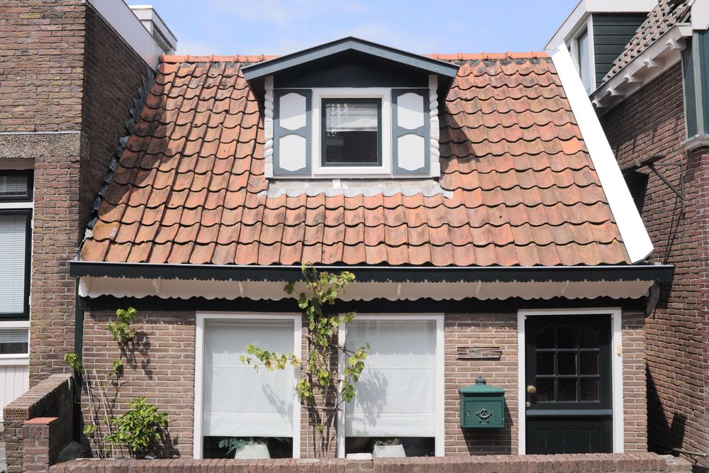 Small Dutch brick house with terracotta tile roof, dormer window, and green mailbox, typical Netherlands residential architecture.