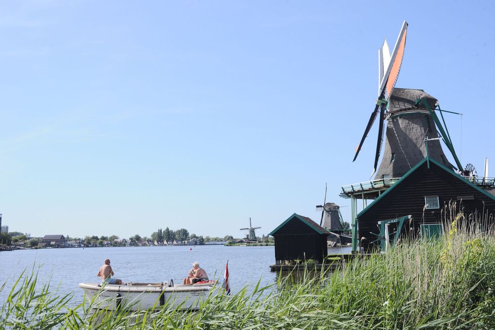 Two people in a small boat on a calm river beside a traditional Dutch windmill at Zaanse Schans, Netherlands.