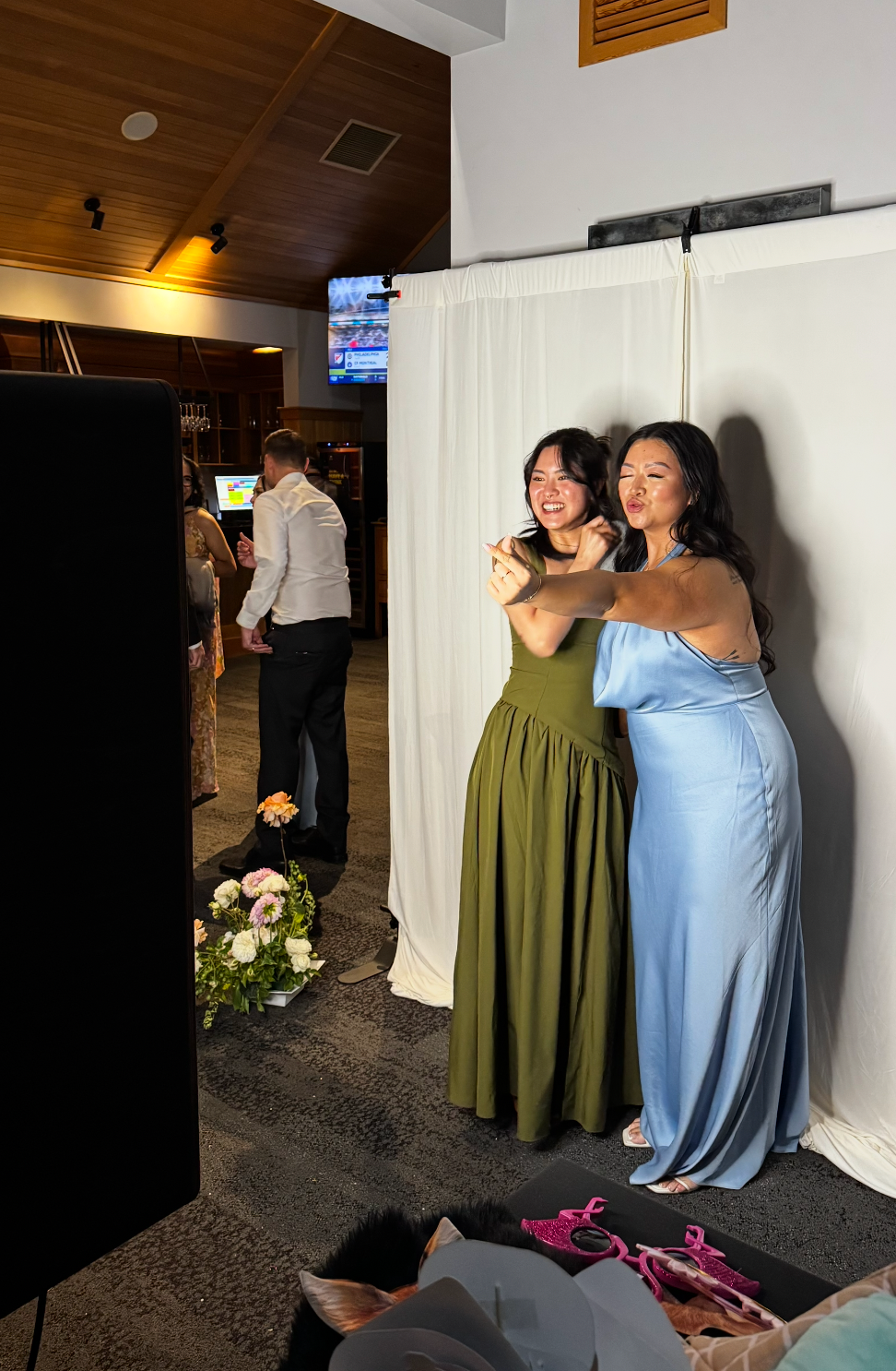 Two women in elegant gowns, olive green and light blue, posing together at a formal event photo booth.