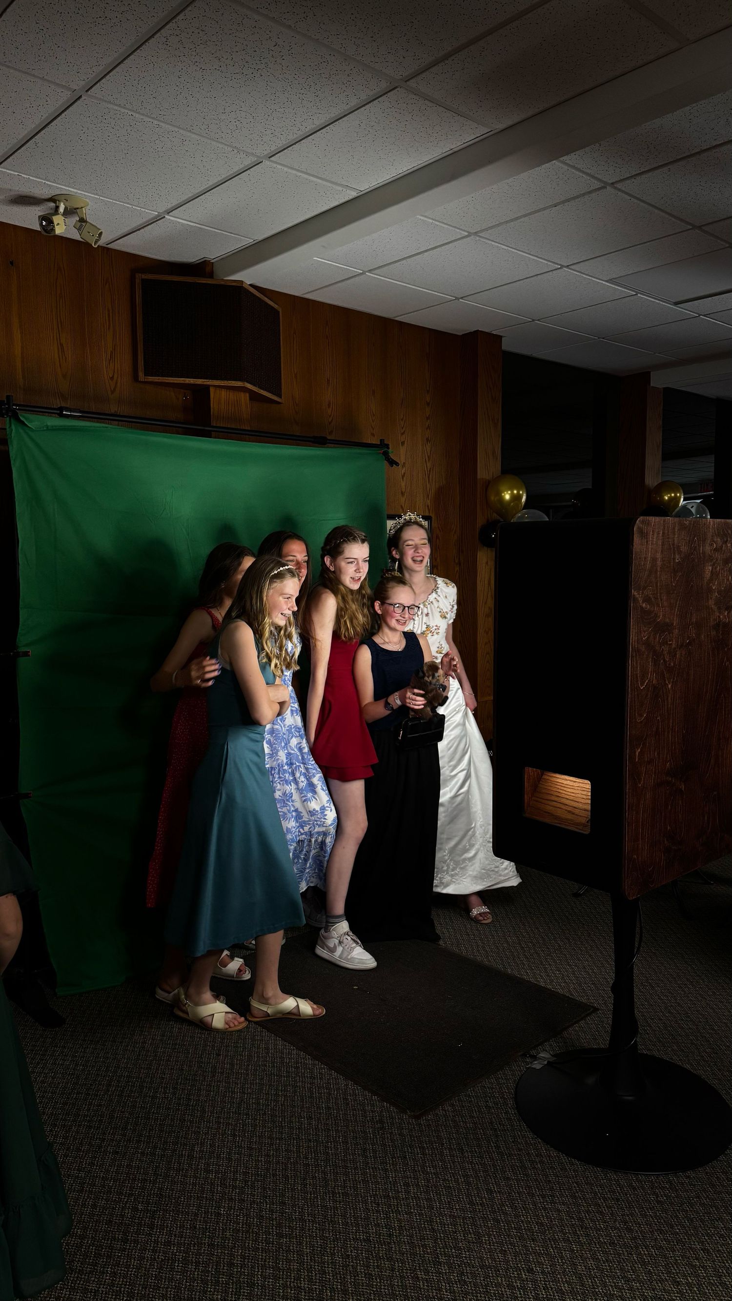 Group of young girls posing in front of a green screen backdrop at a formal event or party.