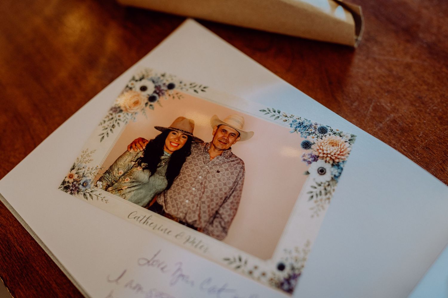 A wedding photo booth picture of a couple in cowboy hats with floral border design on a wooden table.