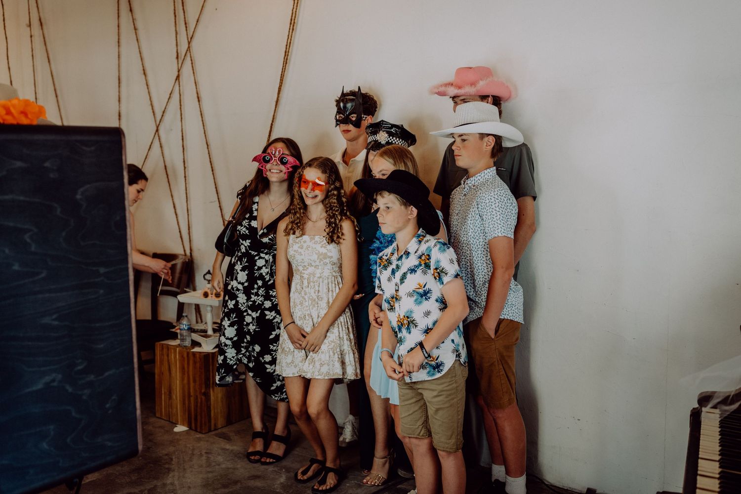 Group of kids wearing fun photo booth props including colorful glasses and hats at a casual indoor party event.
