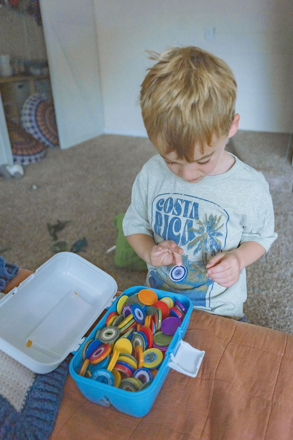 Young blonde boy in Costa Rica shirt sorting colorful toys in a blue container on a table indoors.