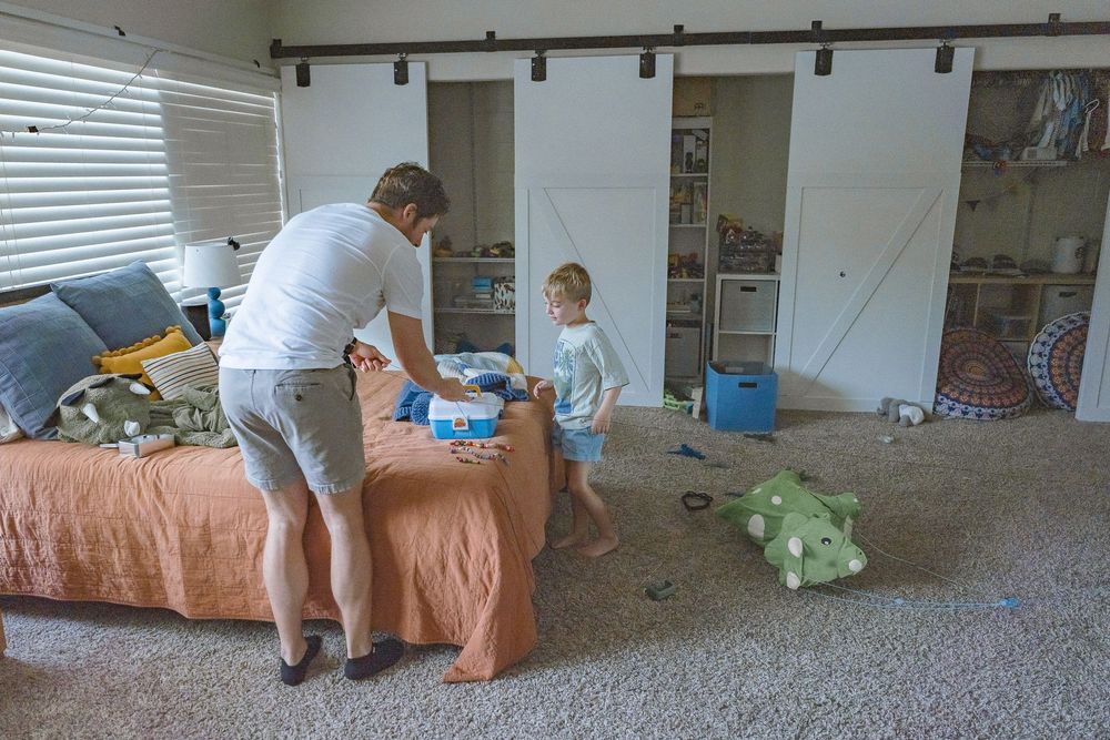 Father and toddler playing in a bright bedroom with barn doors and toys on carpet.
