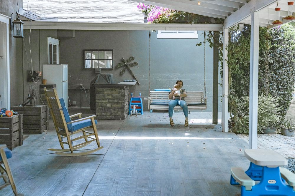 Person relaxing on bench in a covered outdoor patio with rocking chair and garden.