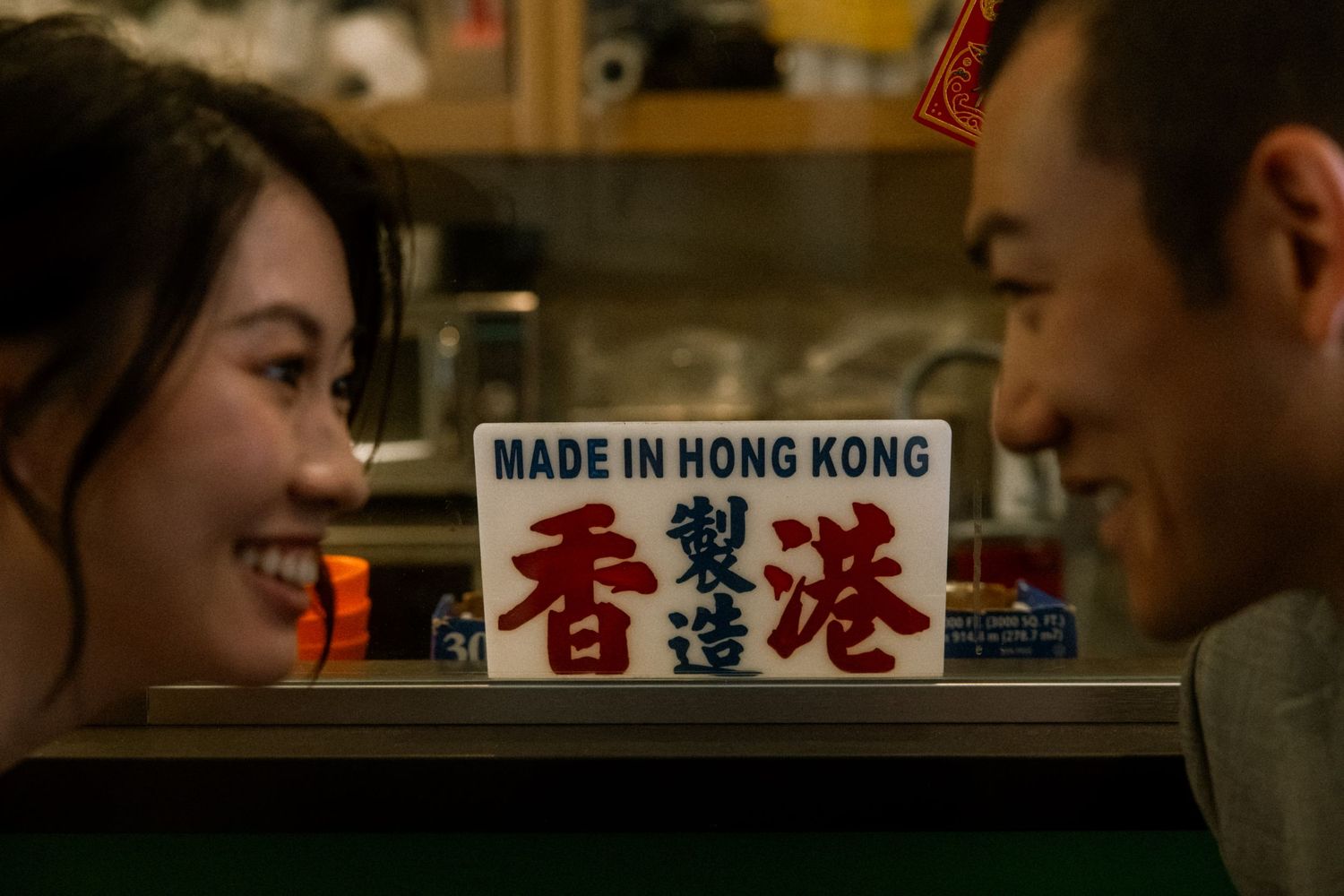 Two people smiling at a counter with a Made in Hong Kong sign in English and Chinese characters.