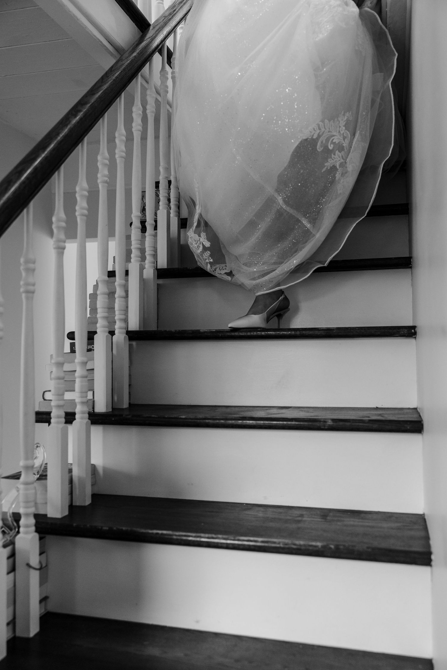 Black and white photo of a wedding dress draped over wooden staircase railing with white balusters.